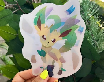 May include: A die-cut sticker featuring a stylized, light yellow creature with large dark eyes and pointed ears. The character has flowing green leaf-like accents on its head and tail, with translucent, layered geometric shapes surrounding it.