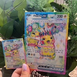 Peut inclure: Deux cartes à collectionner Pikachu ex. La plus grande carte présente une illustration colorée de Pikachu avec le texte "Resolute Heart" et "Topaz Bolt". La plus petite carte reprend le design. Les deux cartes ont un effet holographique arc-en-ciel.