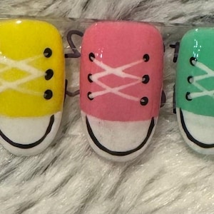 May include: Five miniature nail art designs featuring colourful sneakers with white laces. The sneakers are painted in blue, yellow, pink, green, and purple.