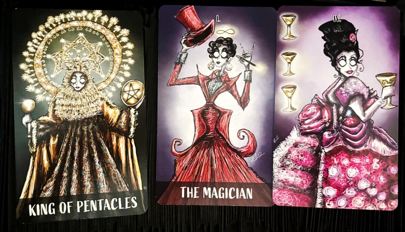 Puede incluir: Tres cartas de tarot con ilustraciones de inspiraci&oacute;n g&oacute;tica. La carta del Rey de Pent&aacute;culos presenta una figura con una t&uacute;nica dorada, una corona y un pentagrama. La carta del Mago presenta una figura con un vestido rojo y un sombrero de copa. La carta del Cuatro de Copas presenta una figura con un vestido rosa sosteniendo una copa dorada.
