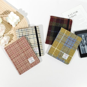 May include: Four rectangular notebooks with textured wool covers featuring various plaid and tweed patterns in red, beige, dark brown, and yellow. Each notebook includes a black elastic closure band and a small white label with text.