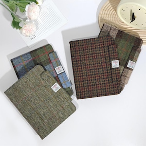 Może przedstawiać: Widok z góry na kilka notatników z tweedu w różnych wzorach i kolorach. Notatniki mają wzory w jodełkę, kratę i pepitkę w odcieniach zieleni, brązu i niebieskiego. Każdy notatnik ma małą etykietę.