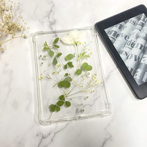 May include: A clear phone case with pressed flowers and leaves inside. The flowers are white and the leaves are green.