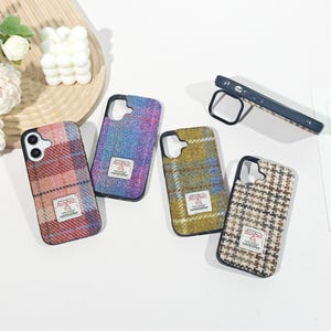 May include: Four smartphone cases with textured fabric backs in plaid and houndstooth patterns, featuring a small rectangular Harris Tweed label on each. The cases have black frames and camera cutouts, with one case shown from the side profile.
