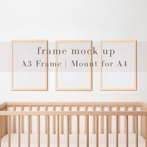 May include: Three wooden picture frames on a white wall above a wooden crib. The frames are empty and have a light wood finish. The text "frame mock up" is written on the wall above the frames. The text "A3 Frame | Mount for A4" is written below the frames.