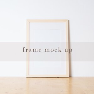 Könnte beinhalten: Ein einfacher Holzrahmen mit einem weißen Passepartout und einem weißen Hintergrund. Der Rahmen steht auf einer hellen Holzoberfläche. "frame mock up" steht in der Mitte des Bildes.