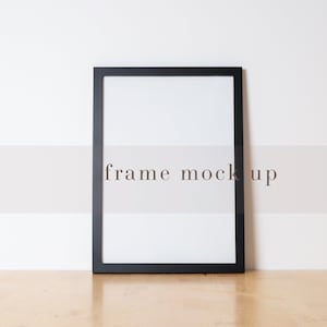 May include: A black picture frame with a white mat and a white background. The frame is sitting on a wooden surface. The text "frame mock up" is visible in the background.