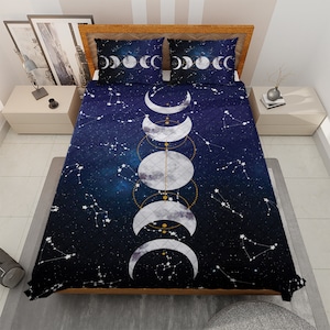 May include: A navy blue quilt with a white moon phases design and gold accents. The quilt features a constellation pattern with stars and a galaxy background.