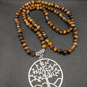 May include: A brown and gold tiger's eye beaded necklace with a silver tree of life pendant. The necklace is on a black background.