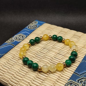 Peut inclure: Un bracelet en perles vertes et jaunes avec des accents dorés. Le bracelet est fait de malachite et de citrine.