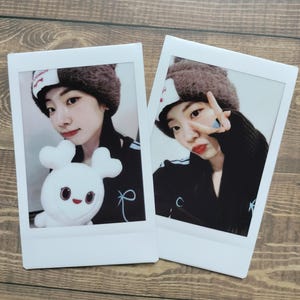 Op de afbeelding: Twee foto's in polaroid-stijl. Eén foto toont een persoon met een bruine, harige hoed en een zwarte jas, die een wit pluchen konijn vasthoudt. De andere toont de persoon die een vredesteken maakt.