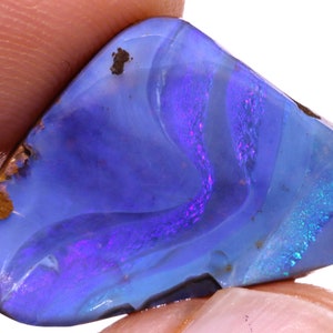 May include: A polished, triangular-shaped boulder opal gemstone featuring a vibrant play of color with deep blue and purple hues, accented by bright cyan flashes and small patches of natural brown ironstone matrix along the edges.