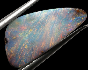 May include: A teardrop-shaped opal gemstone with a blue, green, and red iridescent sheen. The opal is held in tweezers against a black background.