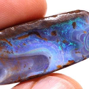 May include: A rectangular boulder opal gemstone featuring a dark brown ironstone matrix with vibrant flashes of iridescent blue, purple, and green color play across the polished surface, displaying natural swirling patterns.