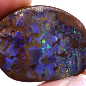 May include: A polished boulder opal gemstone featuring a dark brown ironstone matrix with vibrant flashes of deep blue, violet, and bright neon green color play across its irregular, rounded surface and smooth, glossy finish.