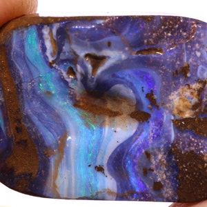 May include: A polished opal stone with a rectangular shape. The opal features swirling patterns of blue, teal, and white, with areas of brown matrix. The stone's surface is smooth and reflective, showcasing a play of color.