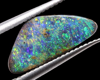 May include: A green, blue, and purple opal gemstone with a rough, irregular shape. The opal is held in place by a pair of silver tweezers.