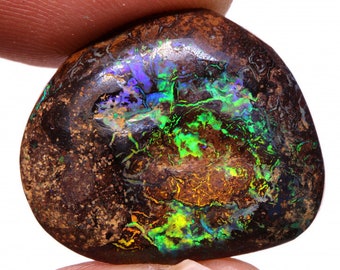 May include: A polished, natural opal gemstone with a dark brown base color. The opal displays vibrant internal play-of-color, including flashes of green, blue, and yellow. The stone has a rounded, irregular shape, showcasing its unique, organic form.