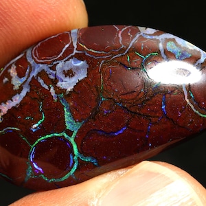 May include: A red, green, and blue opal gemstone with a swirling pattern. The opal is a cabochon cut and has a smooth, polished surface.