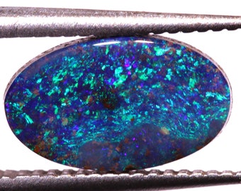 Op de afbeelding: Een blauwe, groene en paarse opaal edelsteen met een gladde, ovale vorm. De opaal is gezet in een zilveren bezel en wordt vastgehouden door een pincet.