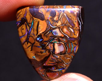 May include: A polished, shield-shaped gemstone with a complex pattern of brown, orange, and black. The stone has iridescent flashes of blue and green, creating a striking visual effect. The gemstone is likely a type of opal.