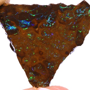 May include: A triangular-shaped piece of opal with a brown base color and a pattern of swirling, textured lines. The opal displays flashes of green and blue iridescence throughout its surface.