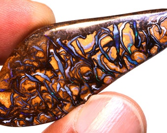 May include: A close-up of a brown, blue and white opal with a swirling pattern. The opal is a rough, natural stone with a smooth, polished surface.