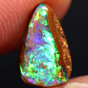 May include: A teardrop-shaped opal gemstone with a green, blue, and purple iridescent sheen. The opal is set in a brown matrix.
