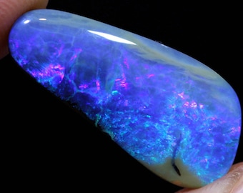 May include: A blue and purple opal gemstone with a smooth, polished surface. The opal has a unique pattern of swirling colors and a dark, almost black, line running through it.