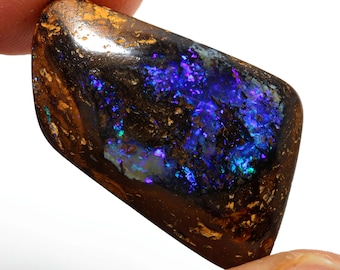 May include: A dark brown, black, and blue opal gemstone with iridescent flashes of color. The opal is cut into a rectangular shape with rounded edges.