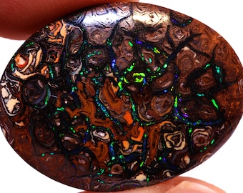 May include: A brown, green, and blue opal cabochon with a swirling, patterned design. The opal is oval shaped and has a high polish.