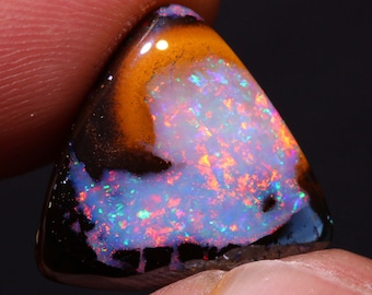 Pode incluir: Uma gema de opala triangular e iridescente com uma matriz preta e marrom. A opala exibe uma variedade de cores, incluindo vermelho, laranja, amarelo, verde, azul e roxo.