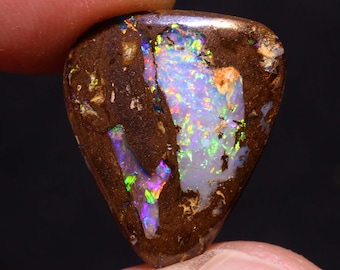 Pode incluir: Uma gema de opala triangular marrom com flashes iridescentes de verde, azul e roxo.
