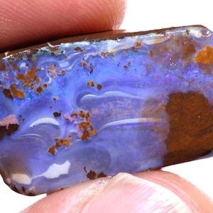 May include: A rectangular boulder opal gemstone featuring a vibrant blue and violet play-of-color with swirling patterns, interspersed with patches of dark brown ironstone matrix and small white inclusions across the polished surface.