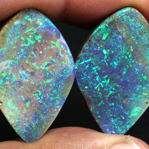 May include: Two teardrop-shaped opal gemstones with a blue, green, and white iridescent sheen.