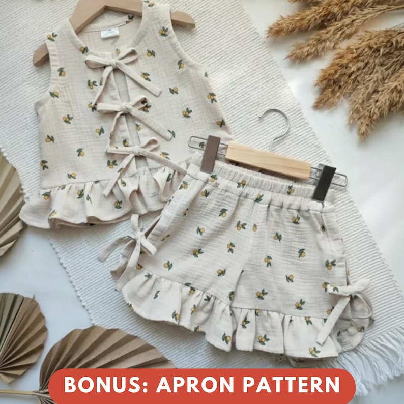 May include: A beige two-piece outfit for children, featuring a sleeveless top with bow ties and ruffled hem, paired with matching shorts. The fabric is patterned with small yellow floral designs. The text "BONUS: APRON PATTERN" is at the bottom.