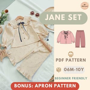 Op de afbeelding: Een beige kinderpyjamaset met een stippenpatroon, ruches en een Peter Pan-kraag. De set bevat een top met lange mouwen en een broek. De afbeelding bevat ook een afbeelding van de pyjamaset en de tekst "JANE SET".