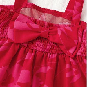 May include: Close-up of a red and pink romper with a floral pattern. The romper features a bow detail at the chest and spaghetti straps. The fabric is gathered at the chest and waist.