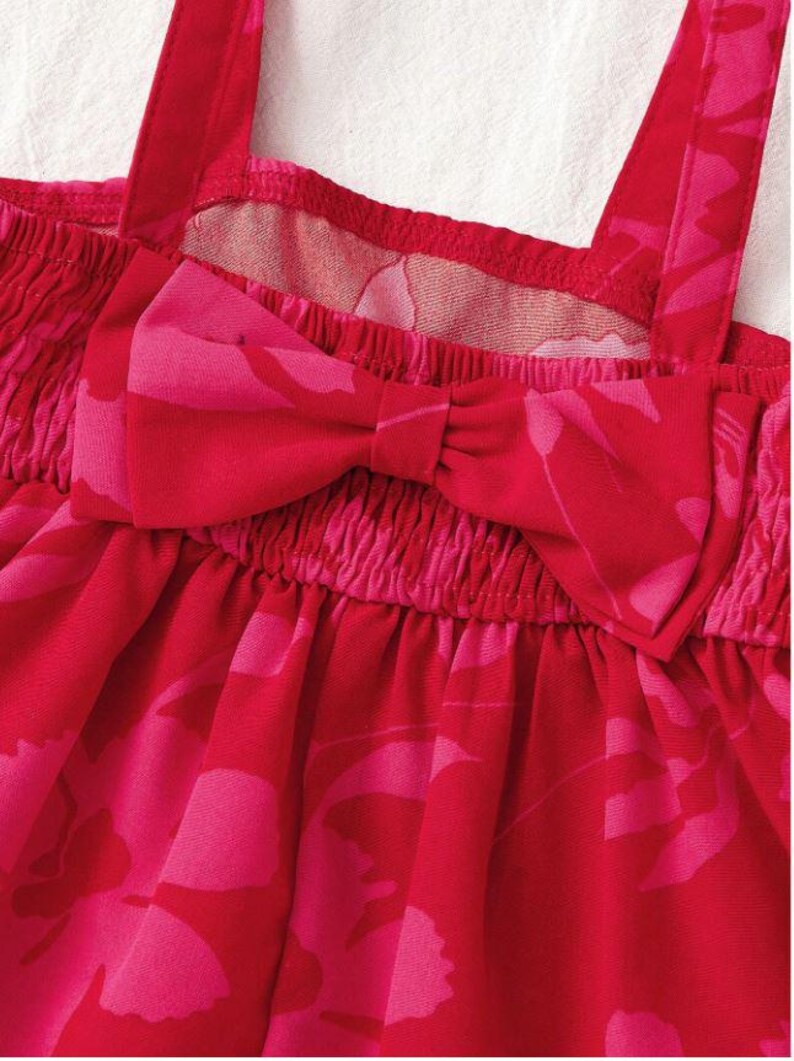 May include: Close-up of a red and pink romper with a floral pattern. The romper features a bow detail at the chest and spaghetti straps. The fabric is gathered at the chest and waist.