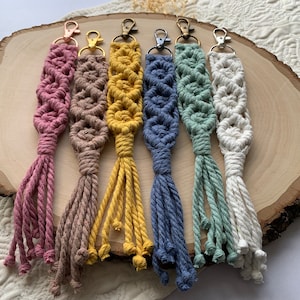 May include: Six colourful macrame keychains with tassels. The keychains are made with a variety of colours, including pink, brown, yellow, blue, green, and white.