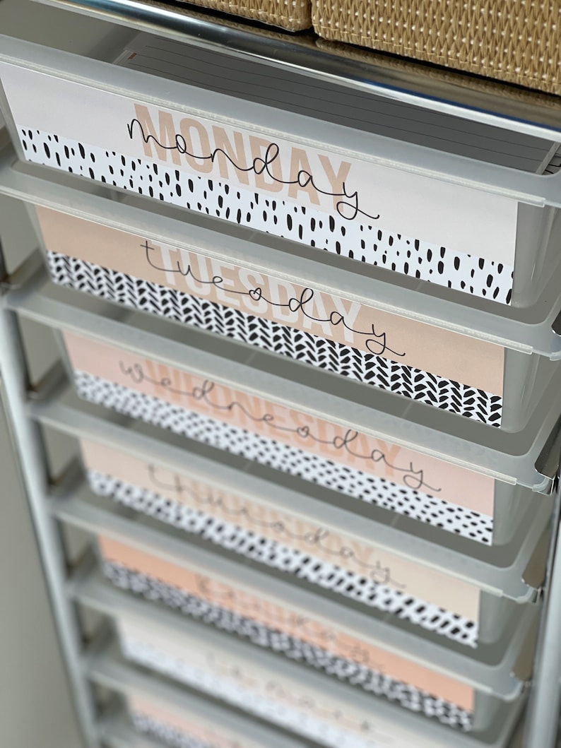 May include: A set of six white drawers with labels for each day of the week. The labels are printed on a peach background with black and white polka dots and a black and white geometric pattern. The labels read "Monday", "Tuesday", "Wednesday", "Thursday", "Friday", and "Saturday".