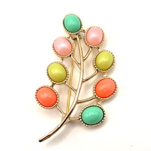 May include: A vintage brooch in the shape of a leaf with a gold-tone finish. The leaf features colorful oval-shaped stones in shades of pink, green, yellow, and orange. The brooch has a pin closure on the back.