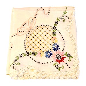 May include: Cream-colored embroidered handkerchief with a floral design. The center features a lattice pattern with colorful flowers in pink, blue, yellow, and red. A pink bow and black dots accent the design, with a lace border.