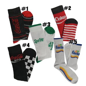 May include: A collection of five pairs of socks with beverage brand logos. The socks feature the Coca-Cola, Sprite, and Fanta logos. The socks are in various colors, including black, red, white, and green. Some socks have striped or checkered patterns.
