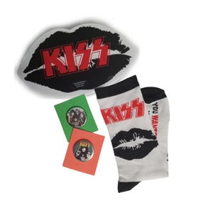 May include: A collection of KISS band merchandise, including a lip-shaped tray with the band's logo in red and black, two pinback buttons, and a pair of white socks with the band's logo and a lip graphic. The socks have the text "YOU WANT".
