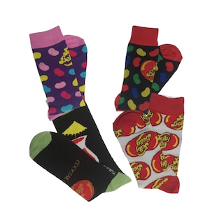 May include: Four pairs of colorful socks. One pair has a purple background with multi-colored dots and pink cuffs. Another pair has a black background with colorful dots and red cuffs. The third pair has a white background with red jelly beans and red cuffs. The fourth pair is black with a cocktail design.