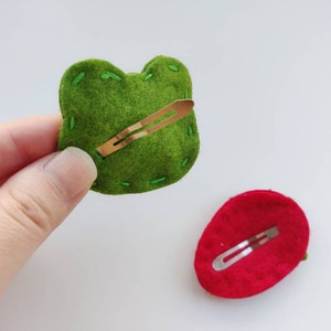 Op de afbeelding: Twee haarclips van vilt, een groene en een rode, met een gouden metalen clip aan de achterkant.