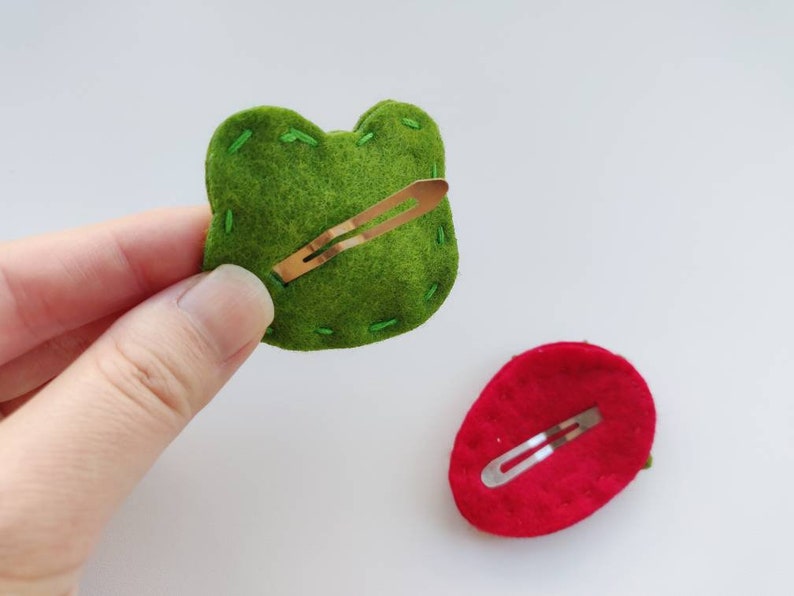 Op de afbeelding: Twee haarclips van vilt, een groene en een rode, met een gouden metalen clip aan de achterkant.