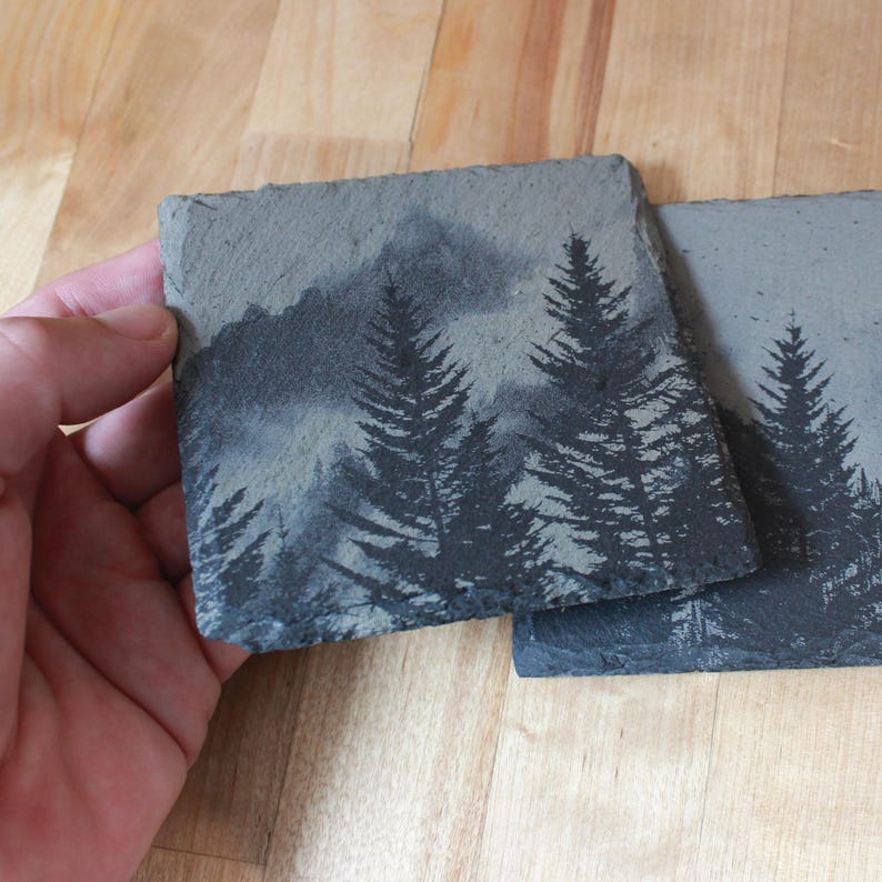 Slate stone drink coaster featuring graphic of a foggy mountain scene etched onto the top surface of the coaster