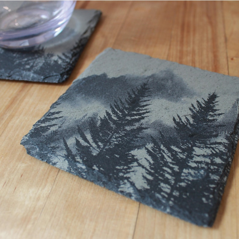 Slate stone drink coaster featuring graphic of a foggy mountain scene etched onto the top surface of the coaster